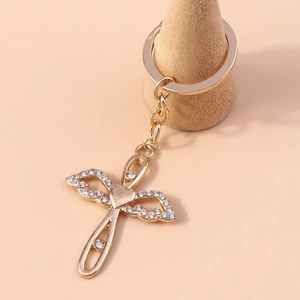 Detail of a golden cross and angel wings keychain encrusted with sparkling white rhinestones