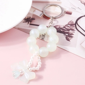 Detail of beaded pearl keychain with matte bow and blue flower pendant on pink background