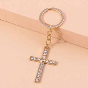 Detail of golden cross keychain with sparkling crystals and a tiny heart on beige pedestal