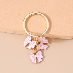 Close-up of golden key ring with three pink enamel bow pendants on aesthetic stand