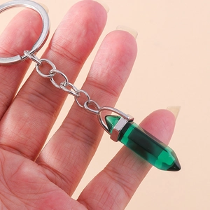 Close-up of a dark green hexagonal crystal keychain held by hand against a soft orange background