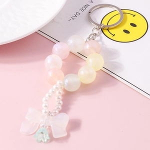Detail of colorful beaded keychain with white bow, pearls and green bell pendant accessory