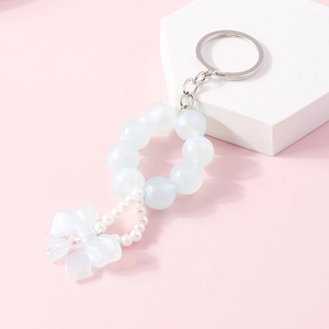 Detail of beaded bow keychain with blue iridescent pearls and silver metal ring