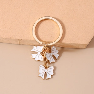 Macro detail of three white enamel bows on a gold-tone metal keychain and ring