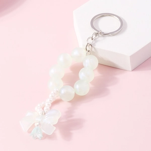 Close-up of pearl beaded keychain with translucent bow and green flower on a pink background