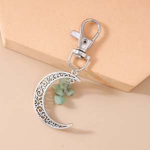 Detail of silver crescent moon keychain with green stones on a geometric stand