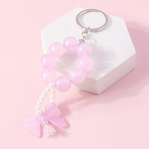 Detailed view of pink beaded bow keychain with pearls and petals on a geometric stand