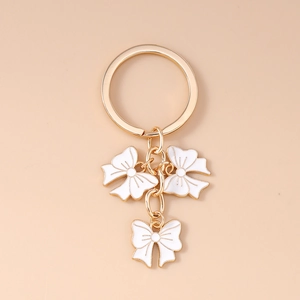 Detail of elegant gold keychain featuring three white enamel bow-shaped charms on a ring