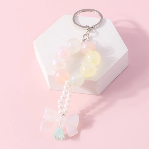 Close-up of beaded keychain with matte bow, colorful beads, and pearl charms on a white stand