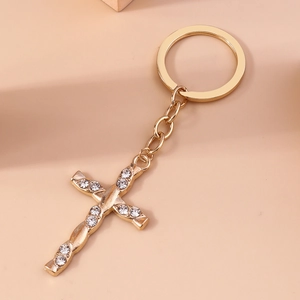 Detail of a gold twisted cross keychain with sparkling white rhinestones on a pink background