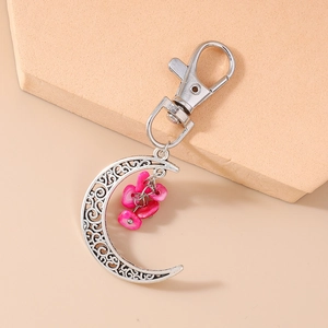Close-up of crescent moon keychain with silver hollow design and pink stones on stone slab