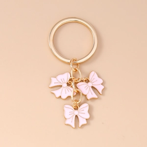 Close-up of golden keychain with three pink enamel bow pendants on a beige background