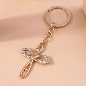 Golden keychain with cross heart wings and white rhinestones on a pink background