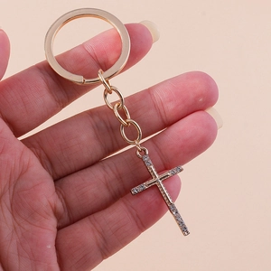 Detailed close-up of a sparkling rhinestone-studded golden cross keychain held in hand