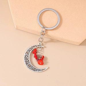 Detail of silver hollow moon keychain featuring vibrant red stones on a beige background