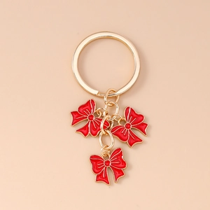 Detail of golden keychain with three red enamel bow pendants on a beige background