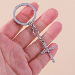 Detailed view of silver rhinestone cross keychain held in hand for size reference
