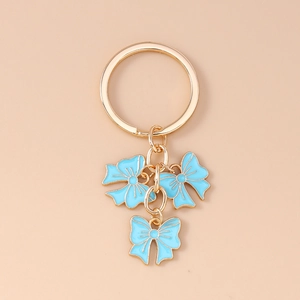 Detail of gold metal keychain with three light blue enamel bow charms on plain background