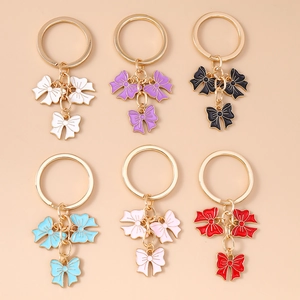 Flat lay of six colorful bow pendant keychains with gold rings on a beige background