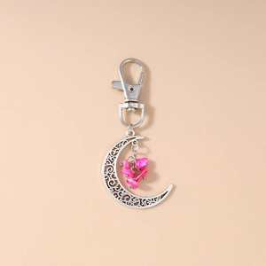 Detail of silver hollow moon keychain with intricate patterns and pink stone charms