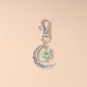 Detail of silver crescent moon keychain with hollow patterns and green turquoise stones