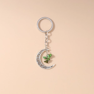 Detailed close-up of crescent moon keychain with green turquoise stones on beige background
