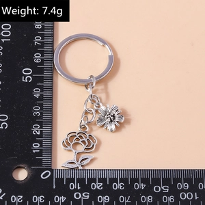 Silver metal floral keychain with daisy and rose pendants measured on a black scale