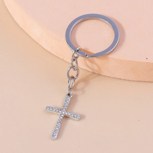Detail shot of a silver-tone cross keychain with sparkling rhinestones on a pink pedestal