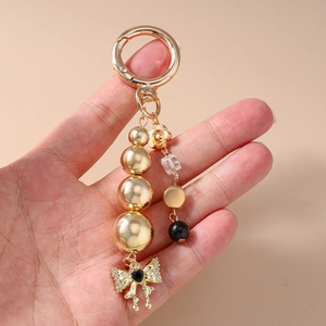 Golden beaded keychain featuring a bow pendant and black heart charm held in hand