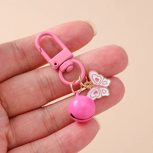 Detailed close-up of pink butterfly bell keychain held by hand on solid background