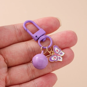 Handheld view of a trendy purple butterfly keychain with bell and lobster clasp
