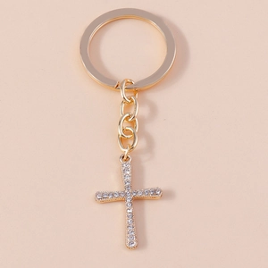 Detail of a sparkling rhinestone-encrusted gold cross keychain on a soft beige background