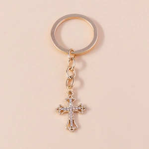 Close-up of golden rhinestone-studded cross keychain pendant with intricate hollow design