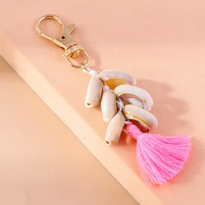 Detail of seashell keychain with golden clasp, natural white shells and pink silk tassel