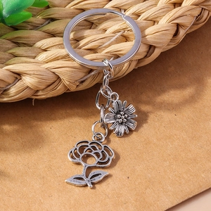 Retro silver metal keychain with daisy and hollow rose charms on rustic woven background