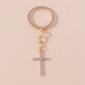 Close-up of golden cross keychain with shimmering white rhinestones on a warm beige backdrop