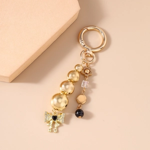 Detailed view of a golden bead keychain with a black heart and bow pendant on pink stones