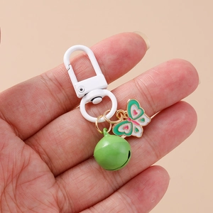 Close-up of hand holding a butterfly pendant keyring with green bell and white clasp