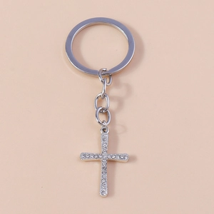 Detailed view of a silver metal cross keychain with sparkling white rhinestones on light background