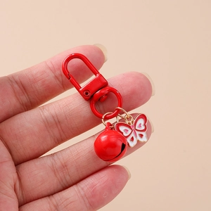 Close-up of red enamel butterfly charm and matching metal bell on a lobster clasp keychain