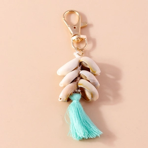 Detail of seashell keychain with mint green tassel and gold clasp on beige background