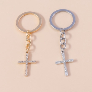 Polished gold and silver cross keychains with clear rhinestones on beige background