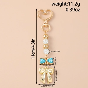 Vue détaillée du porte-clés à nœud bleu avec fermoir coeur et perles dorées sur fond rose