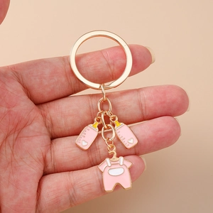Detail view of pink baby bottle and onesie charms on a golden metal keychain held in hand