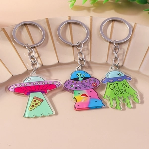 Three acrylic UFO and alien keychains with quirky cartoon designs on textured background