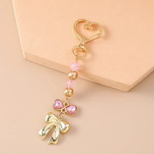 Détail de la perle en cristal rose et du pendentif nœud doré sur le porte-clés en cœur