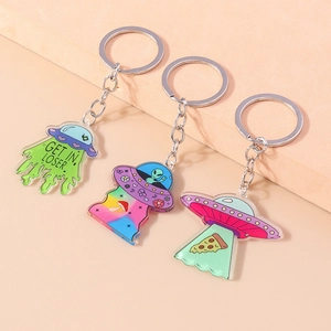 Three acrylic UFO keychains with alien and pizza motifs on a peach background