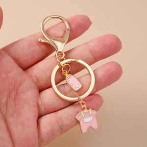 Handheld view of pink enamel baby bottle and romper pendants on a gold metal keychain