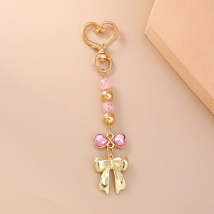 Détails de perles roses craquelées et pendentif nœud doré sur un porte-clé cœur