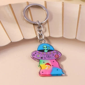 Detail view of acrylic UFO keychain with green alien and rainbow pattern on a ceramic tray